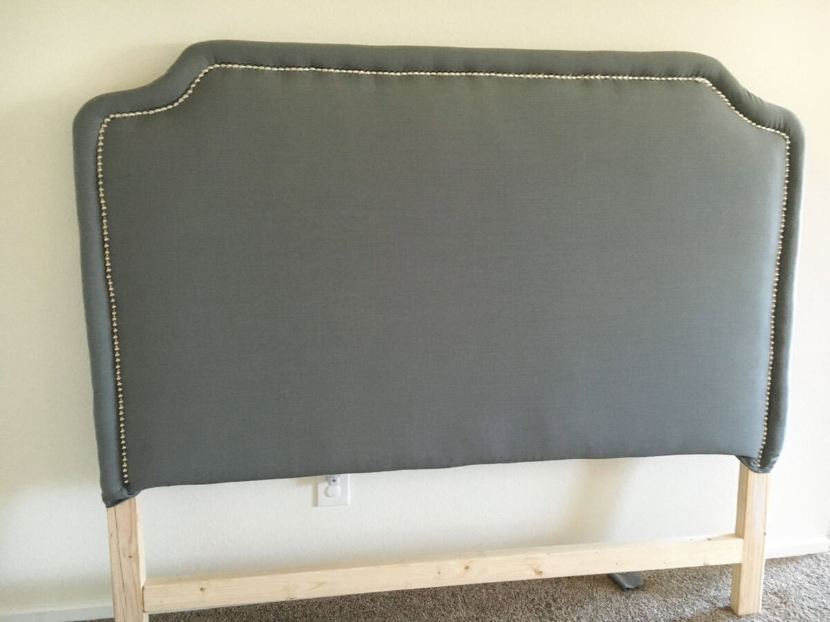 The final headboard with gray fabric and nailhead trim against the wall.