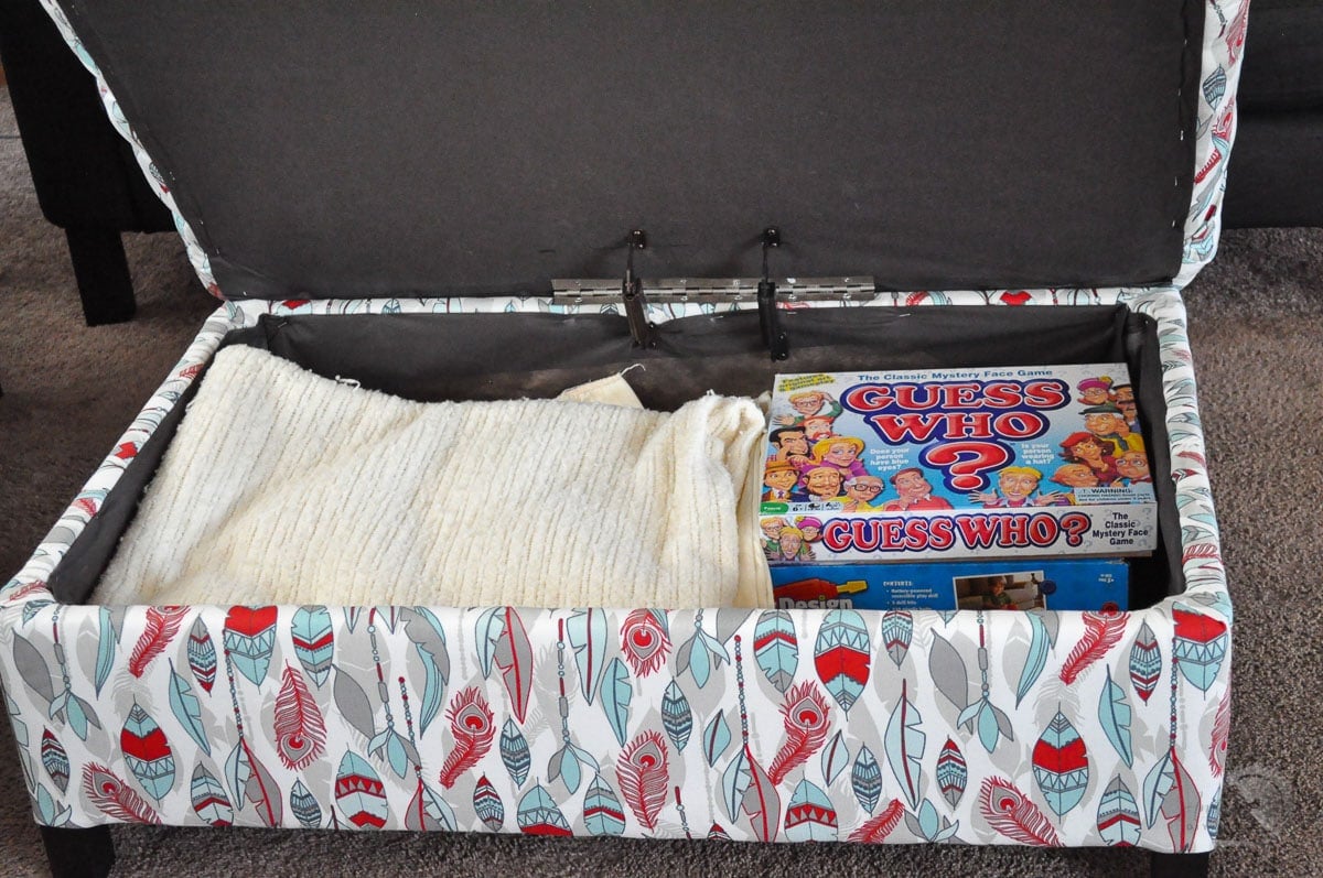 open upholstered storage ottoman with blanket and games inside