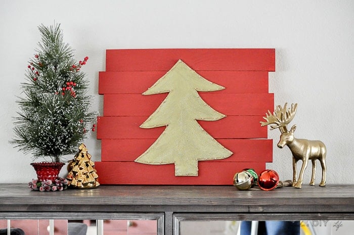 DIY Christmas wall decor with green Christmas tree on red plaque on console table with other Christmas decorations.