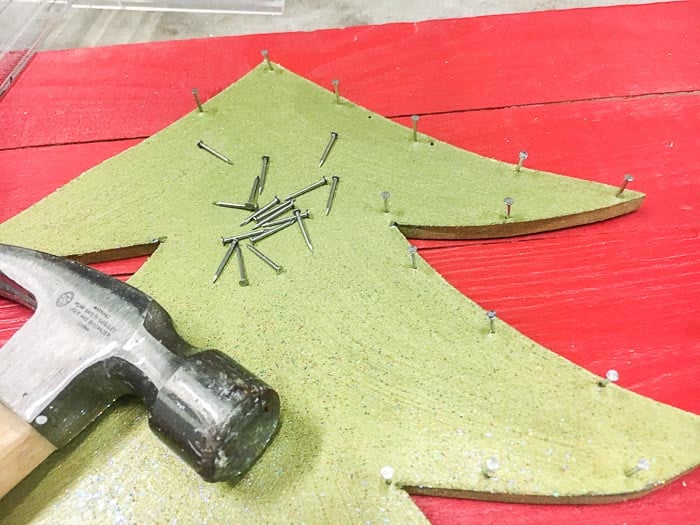 DIY Christmas tree cut out on red background with hammer and nails