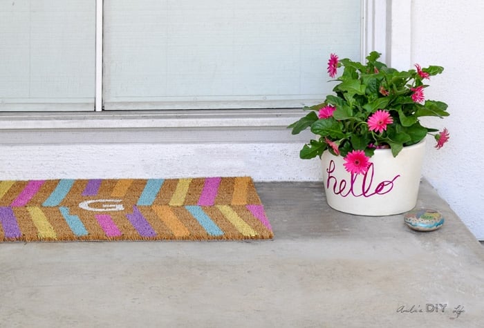 Colorful doormat and whimsical planter at the door of a small front porch