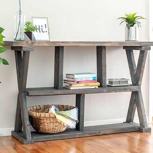 DIY Rustic X-leg Console table that is easy and quick to build with the Free plans. This DIY Entryway table with shelves is made using structural lumber so it's great for your budget too!