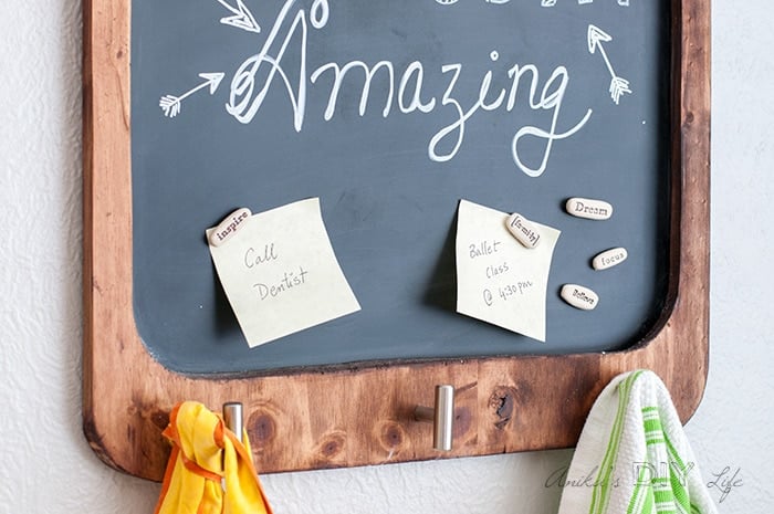 Close up view of the magnetic chalkboard with doodle and rock magnets. Kitchen towel and apron hanging on the knobs