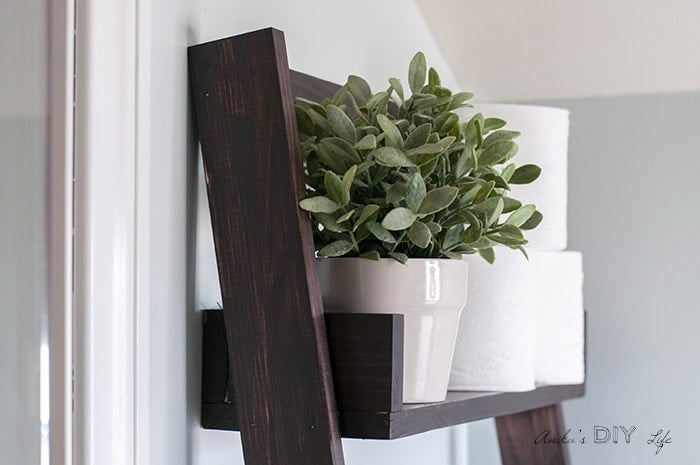 Flower pot with faux greenery on floating ladder shelf.