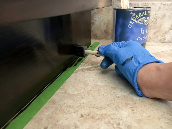 Applying stain near the floor with tape on the floor for masking.