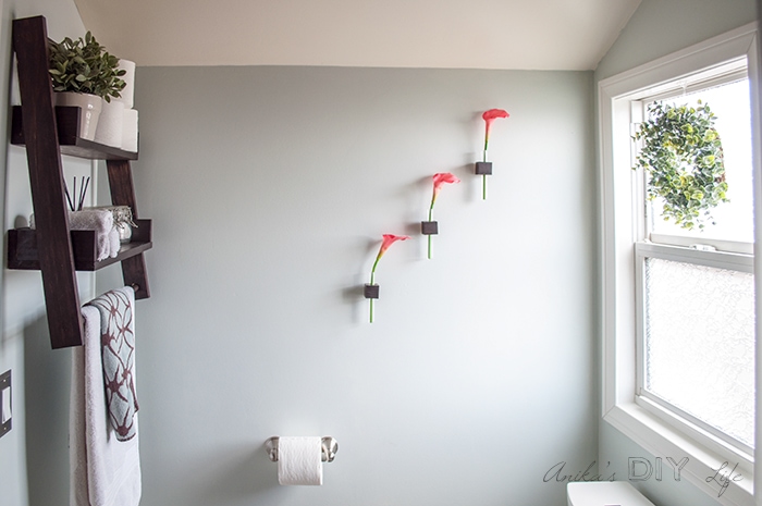 Small bathroom decorating ideas with hanging ladder shelf, test tube vases on wall and wreath in window