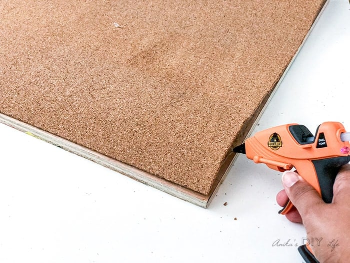 Using hot glue to glue edges of cork roll for DIY cork bulletin board