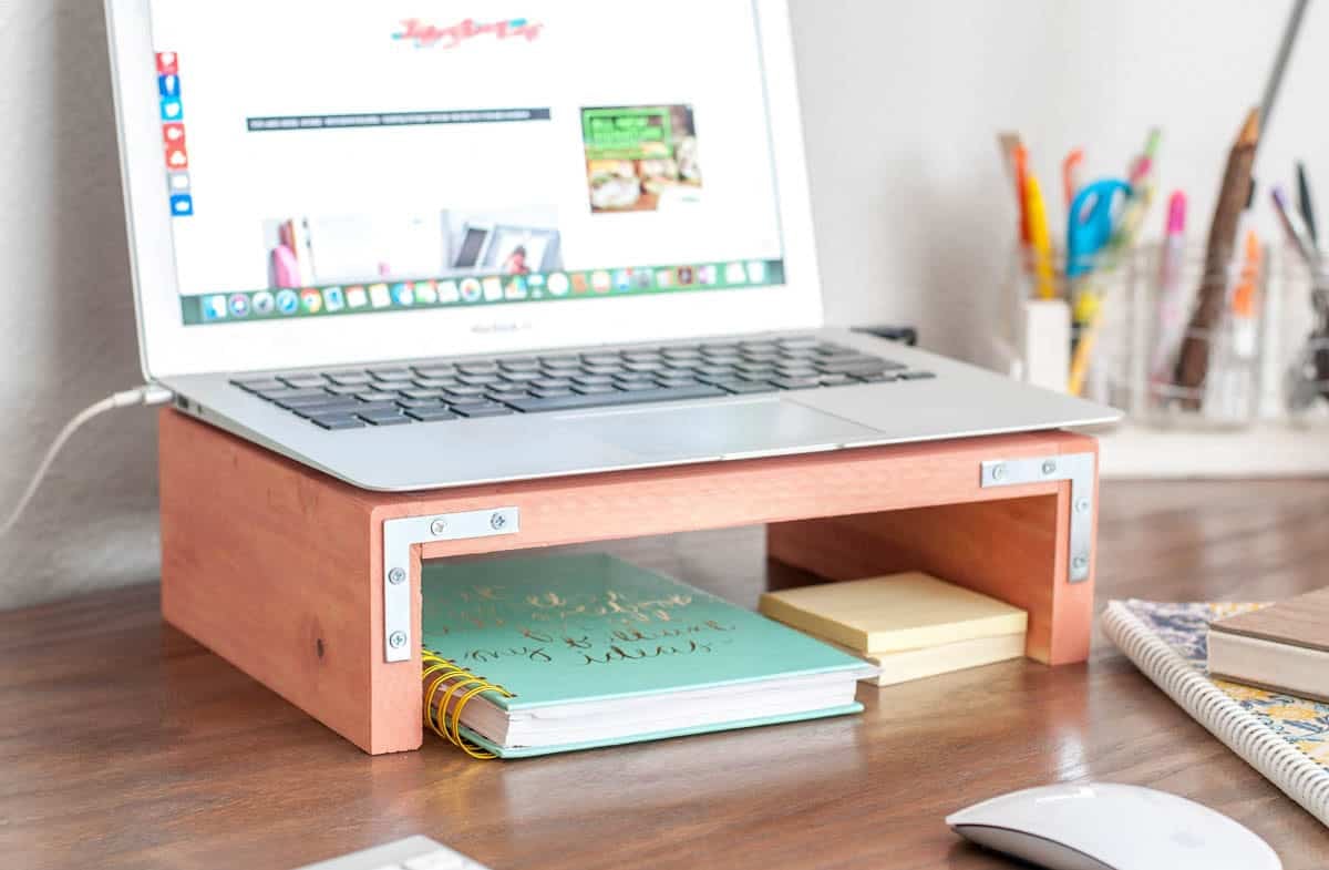 Scrap wood laptop stand on a desk with laptop on it and notebook and post its underneath