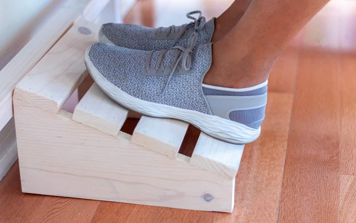 Wood foot rest under a desk with woman's feet resting on it.