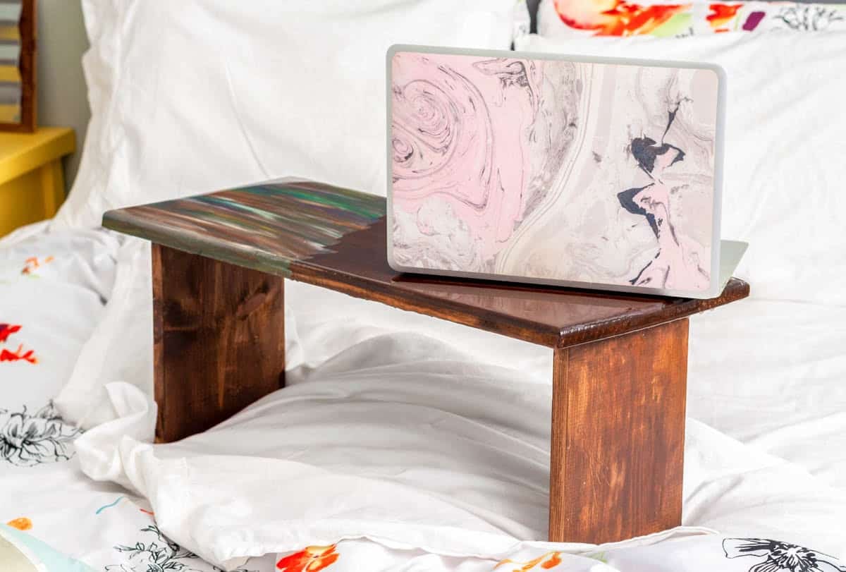 Wood laptop desk with colorful paint detail sitting on a bed