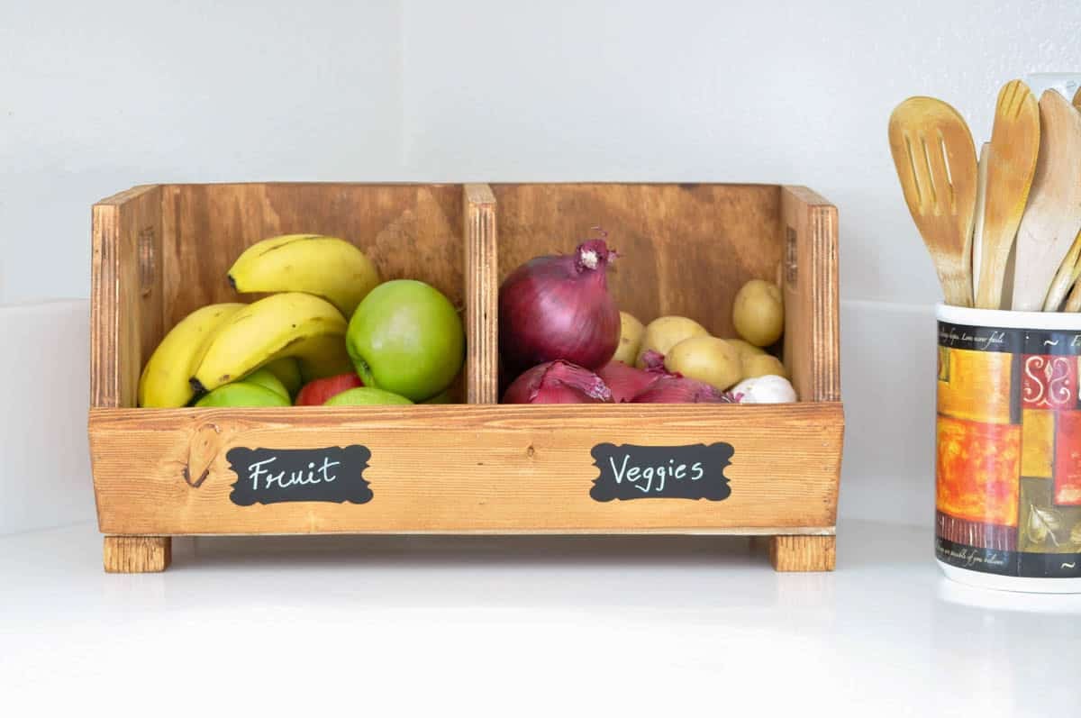 Divided vegetable bin on kitchen counter with fruit and root vegetables.