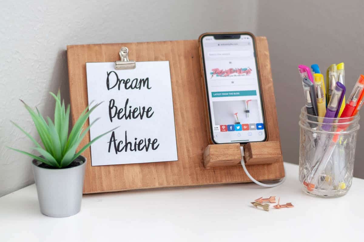 DIY phone stand made with scrap wood holding a phone and a sign that says dream believe achieve
