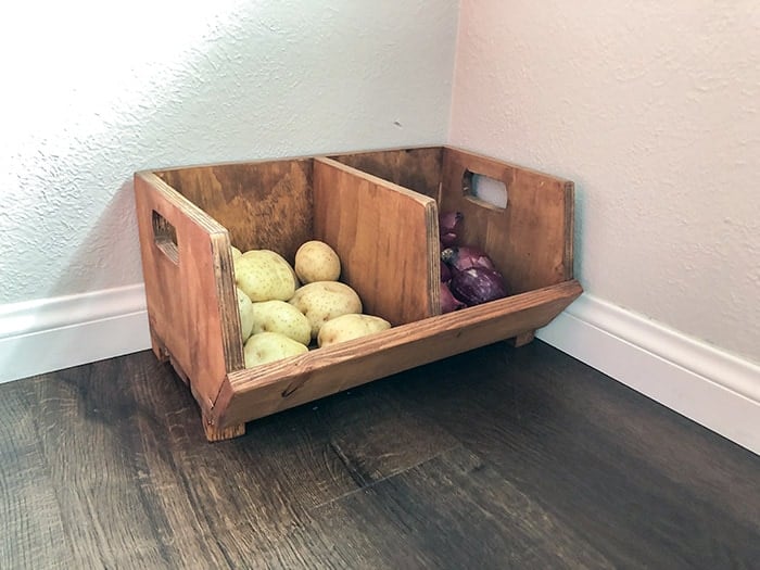 Old two bin divided vegetable bin on the floor with onions and potatos