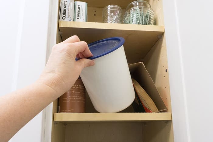 Removing white canister from kitchen cabinet.