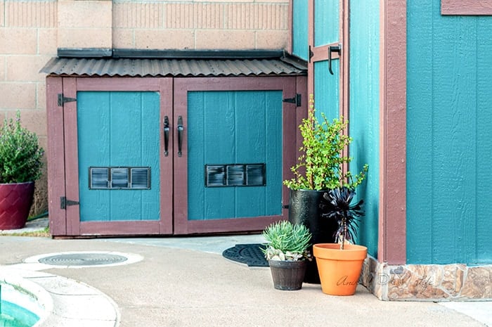 Pool equipment shed painted teal and dark brown with plants in fromt