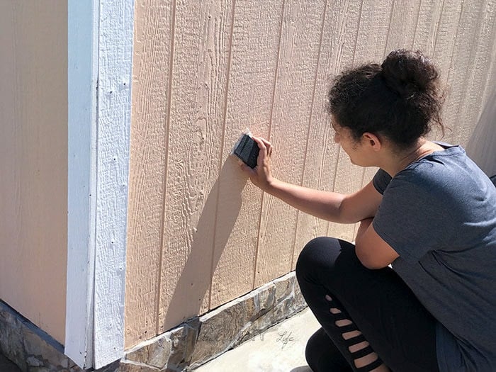 sanding entire shed using a sanding block before giving it a makeover