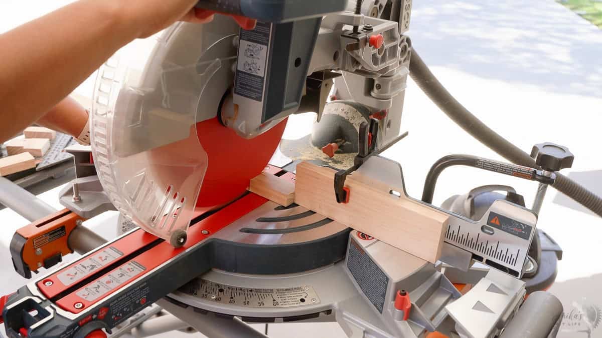 Cutting 1x2 boards with a miter saw and stop block to make a table top book rack