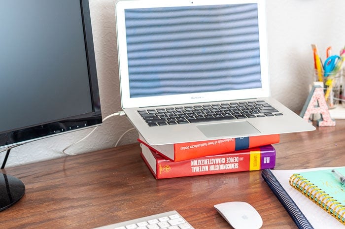 Laptop on desk sitting on top of 2 books to make it higher