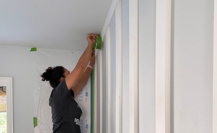 applying painters tape to paint board and batten wall with paint sprayer