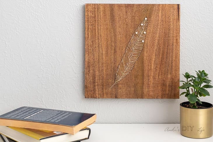 DIY wire and wood art on wall with books and plants on trable