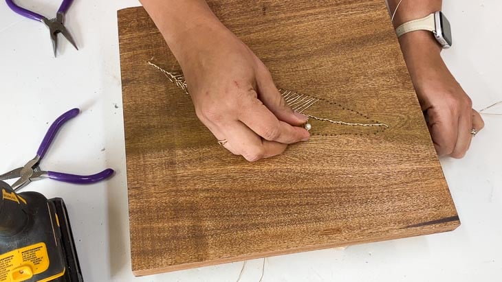 Adding pearls to the DIY wire feather art on wood