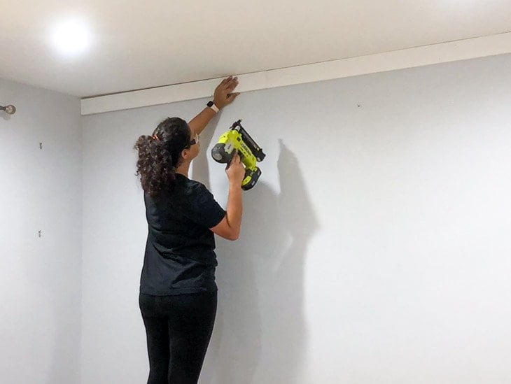 Woman attaching board and batten to wall using nail gun
