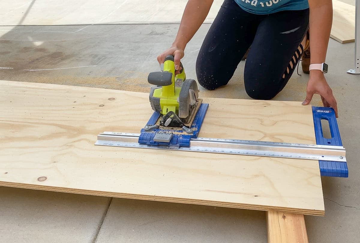 Anika cutting plywood on the driveway floor using a kreg rip cut and circular saw for the desk