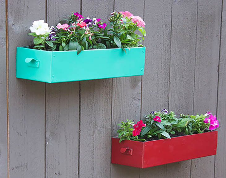 Red and teal metal drawers used as planers on a fence
