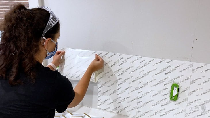 woman applying the Musselbound adhesive tile mat to the wall