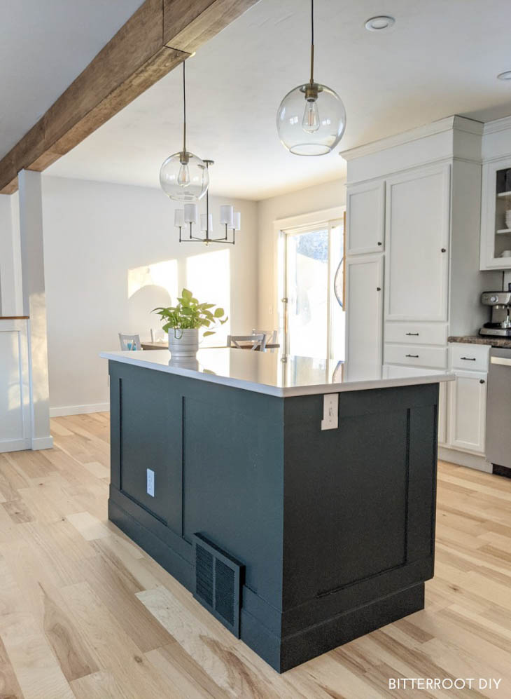 dark green kitchen island with trim in kitchen with wood ceiling beam.