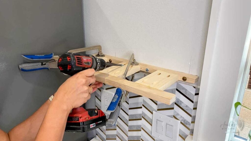 Woman attaching the brace to the wall using pocket hole screws for a floating shelf in the kitchen
