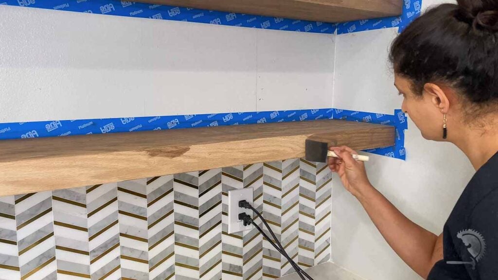 woman staining floating shelves in the kitchen