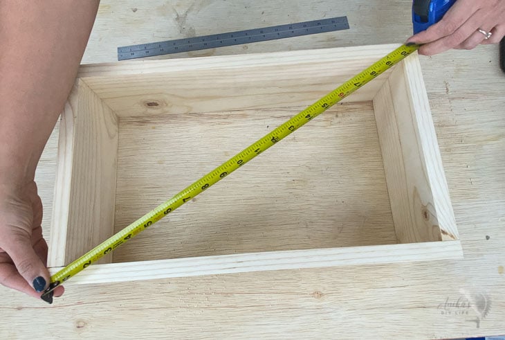 Woman checking the other diagonal of a box using a tape measure to check if it is square.