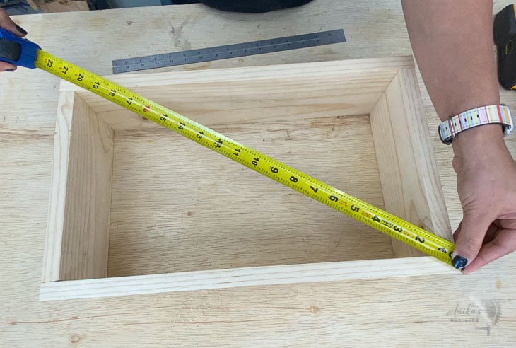 Woman checking the diagonal of a box using a tape measure to check if it is square.