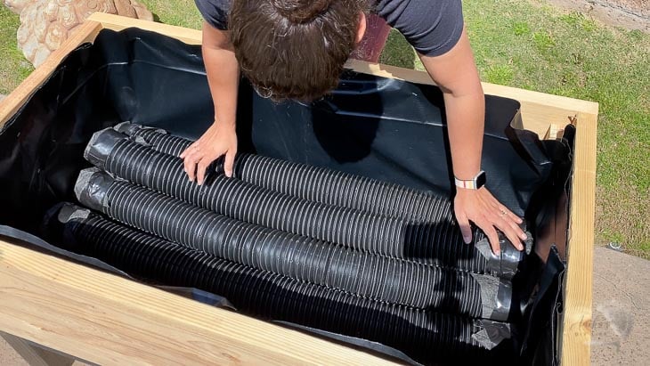 woman laying the corrugated perforated pipes inside the planter to make the DIY self watering raised garden bed