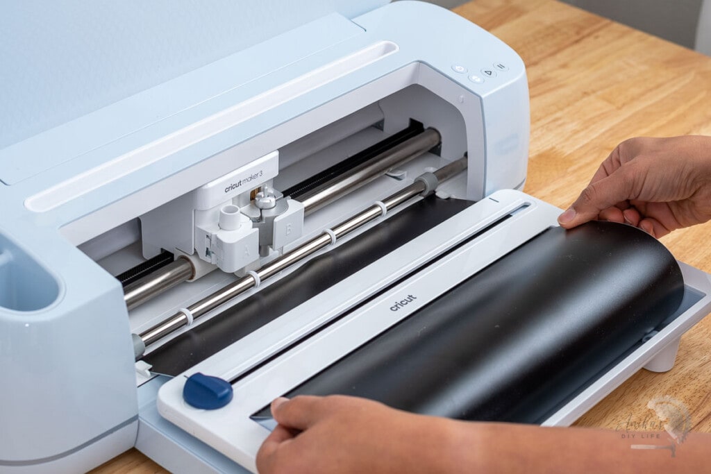 Woman loading black vinyl on the Cricut Roll holder set up on a Cricut Maker 3