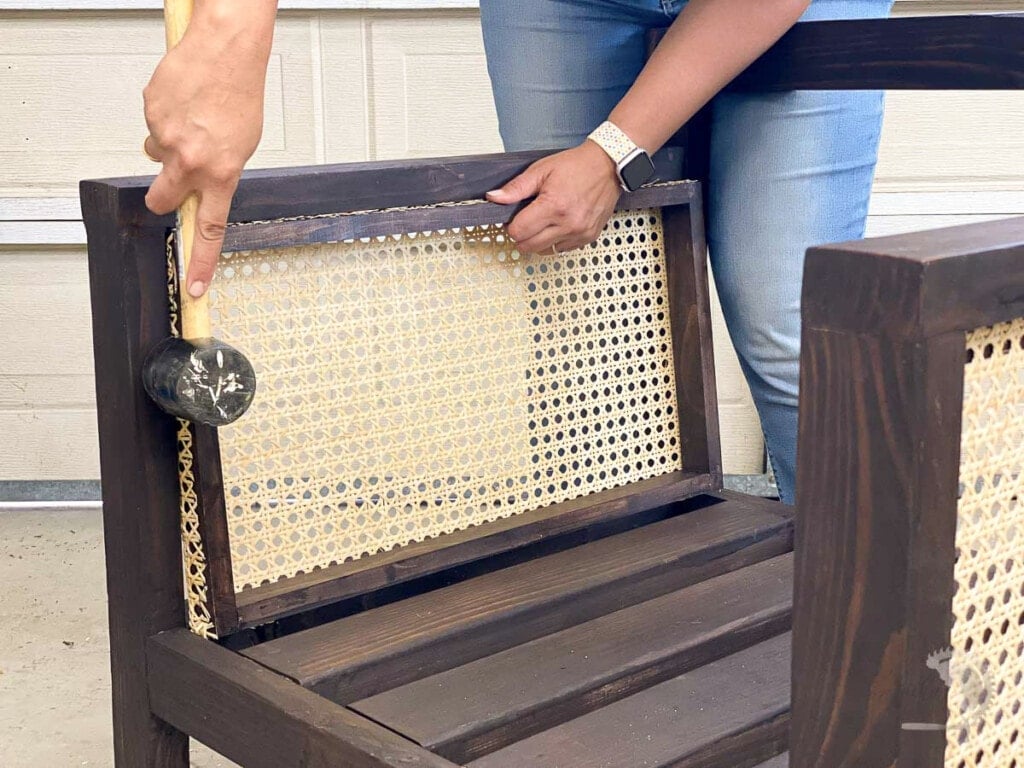 woman using a mallet to tap the cane webbing frame into the arm of the chair