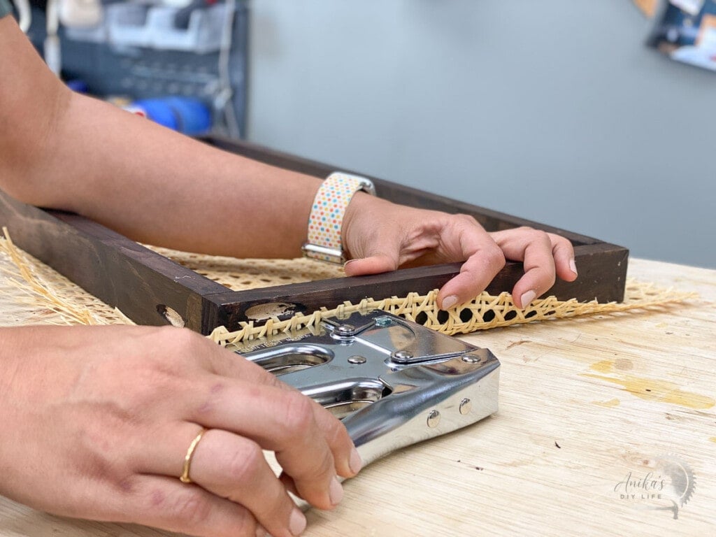 Woman attaching cane webbing to a brown wooden frame using staple gun