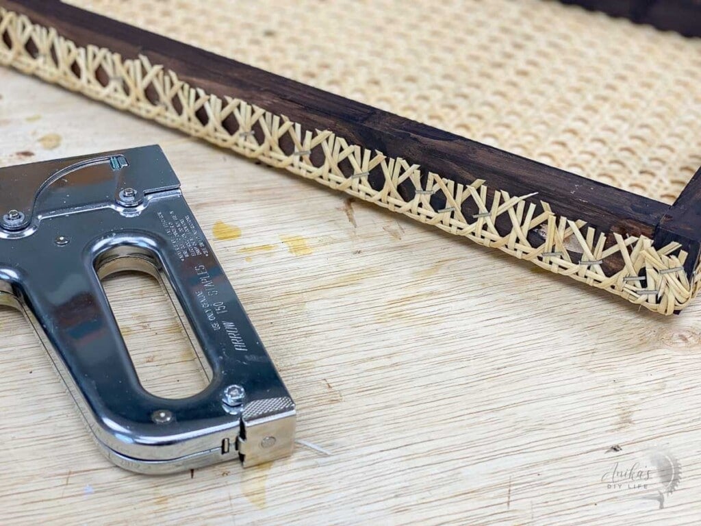 close up of all the staples holding the cane webbing to the brown wooden frame