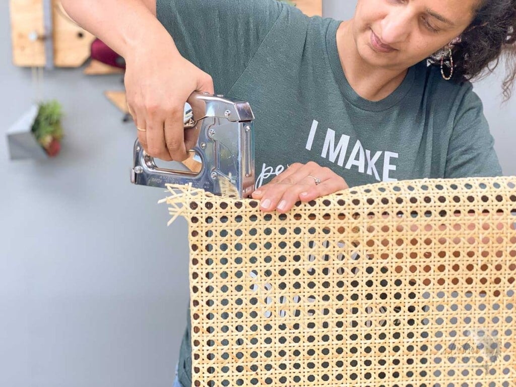 Woman attaching the second side of the cane webbing to the brown frame with a staple gun