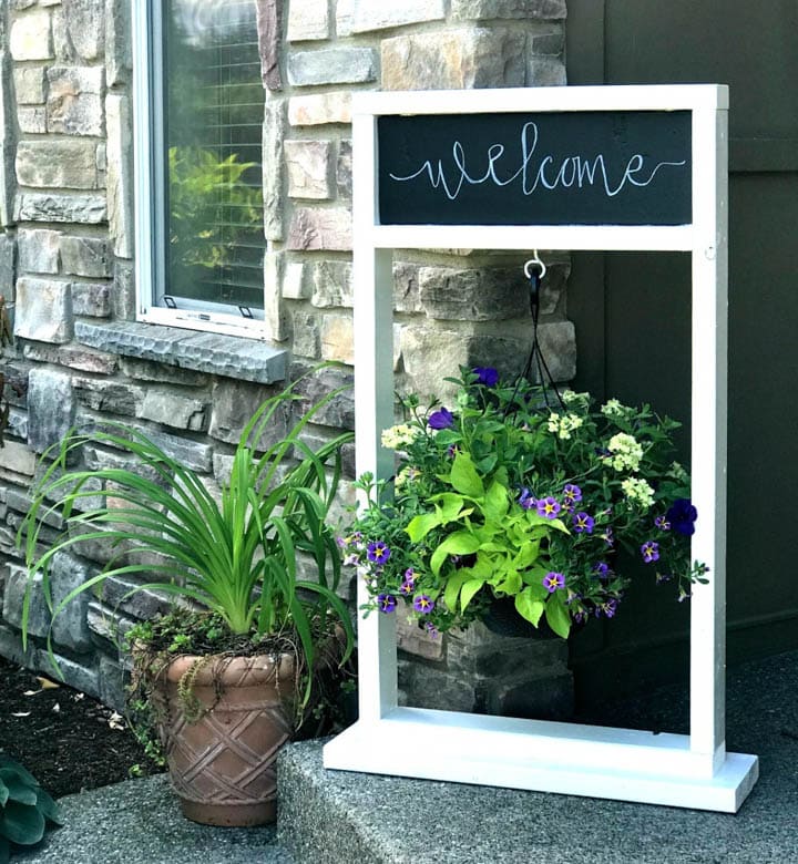 wooden DIY plant stand with hanging plant and chalkboard with welcome written on it