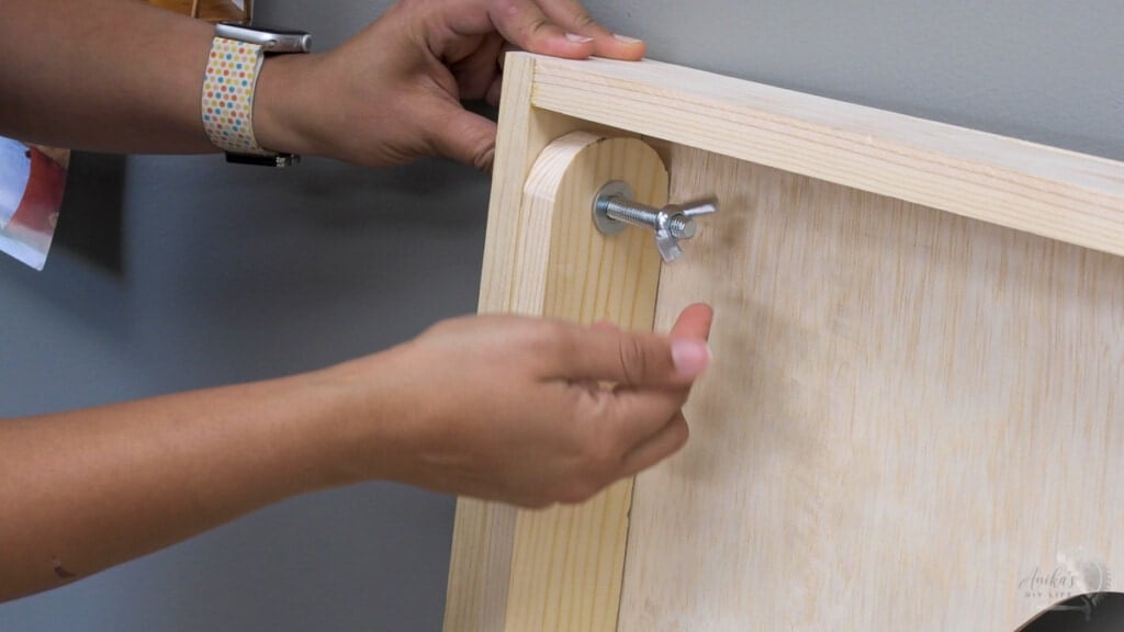 Woman attaching legs to cornhole board using carriage bolt and wing nuts