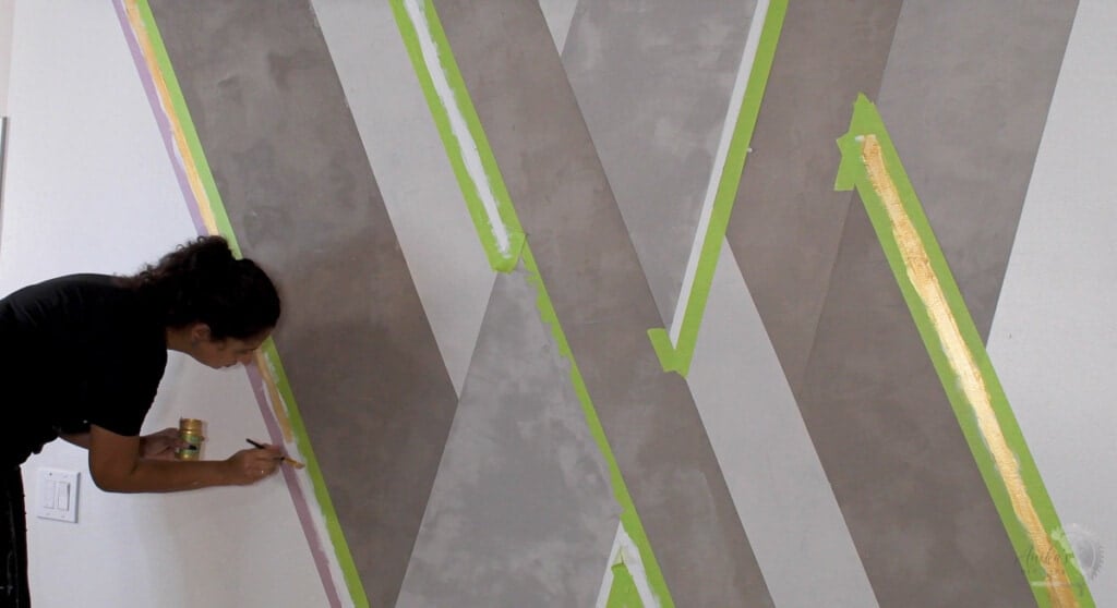 woman painting a gold stripe on a cement accent wall