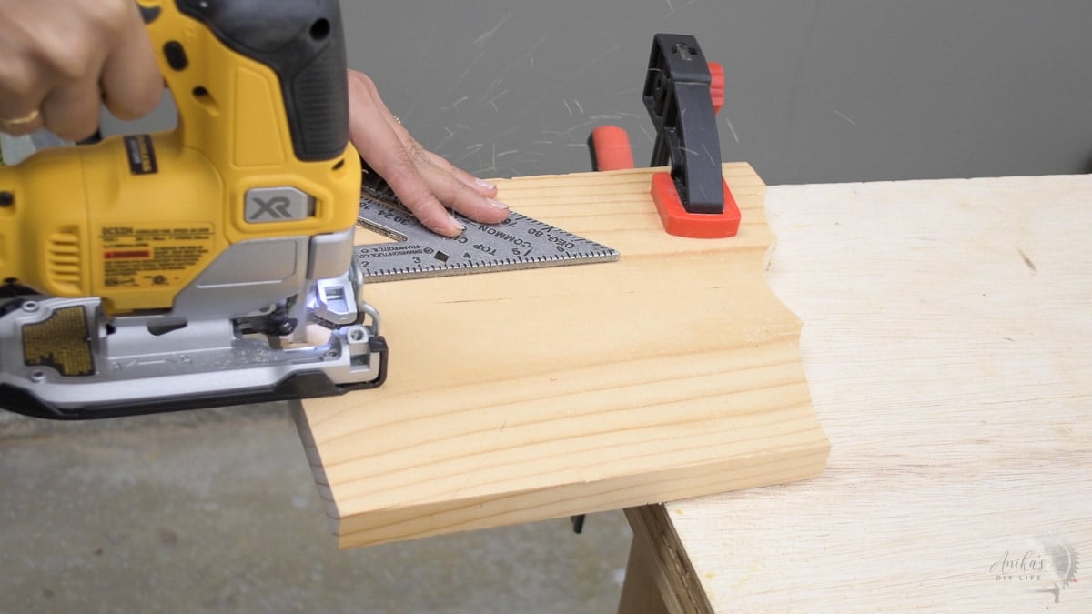 using a speed square to guide a jigsaw to cut a straight line on a board clamped on a workbench