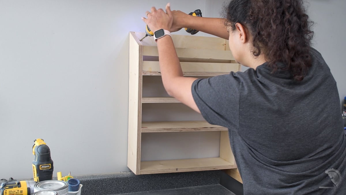 woman attaching the sandpaper storage organizer to the wall.