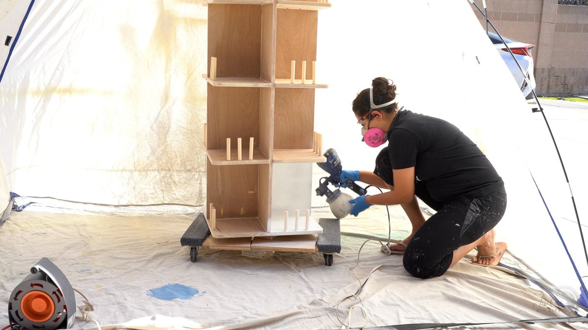woman painting bookshelf with paint sprayer