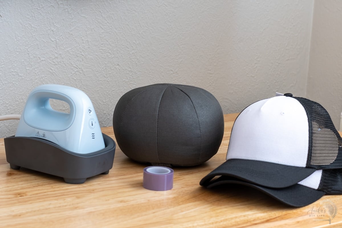 Cricut hat press, hat form, heat resistant tape and hat blanks on table