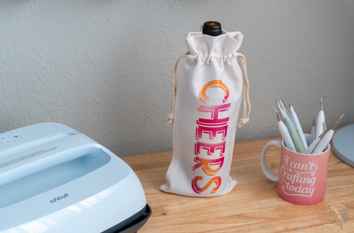 Wine bottle in bag decorated with infusible ink next to EasyPress 3 and tools.