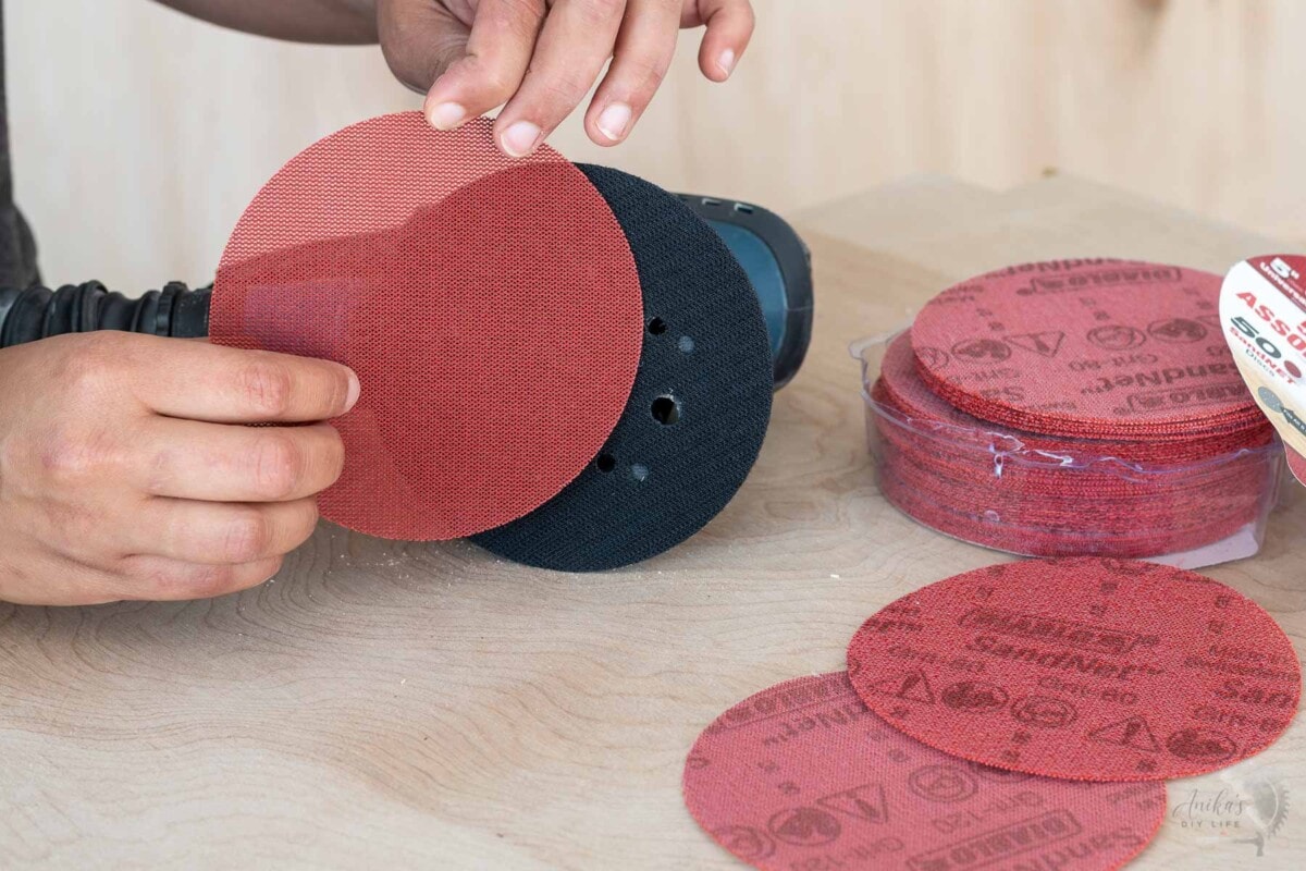 woman attaching sandnet disc to the orbinal sander on a workbench.