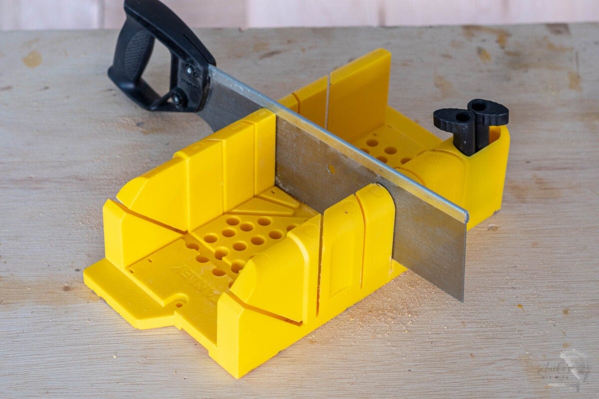 Miter box on a workbench with hand saw and cam pins.